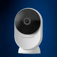 Weiße Homematic IP Überwachungskamera mit schwarzem Objektiv vor blauem Hintergrund.