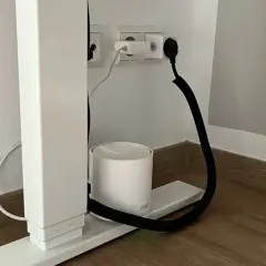 Ein weißer Router steht auf einem Sockel, während ein schwarzer Kabelkanal hilft, das Kabel unsichtbar zu verlegen.