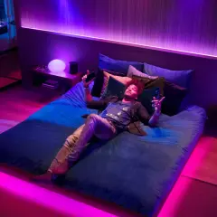 Mann liegt im Bett, umgeben von Philips Hue Lichtern, die sich im Takt von Spotify-Musik synchronisieren.