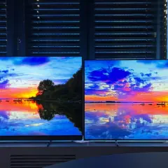 Zwei LG Ambilight Fernseher zeigen einen dramatischen Sonnenuntergang über dem Wasser. Die Lichter spiegeln sich im ruhigen See.