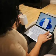 Person mit Tasse hält einen Laptop, auf dem Windows 11 installiert ist.