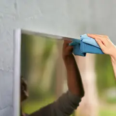 Hand wischt mit Mikrofasertuch über den Bildschirm. Einfache Hausmittel für Bildschirm reinigen.