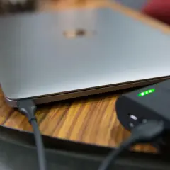 Ein Laptop wird mit einer Powerbank geladen. Die Ladeanzeige der Powerbank leuchtet grün.