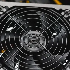 Nahaufnahme eines Lüfters eines PC-Netzteils, bereit für den psu test. Gelbe Kabel im Hintergrund.