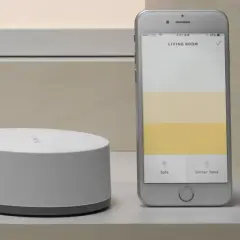 Ein Smartphone zeigt eine App zur Steuerung von adaptiven Licht. Daneben ein weißer Hub.