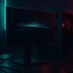 Ein dunkler Raum mit einem flackernden Bildschirm, der digitale Störungen zeigt. Daneben steht ein Computergehäuse, beleuchtet von rotem Licht.