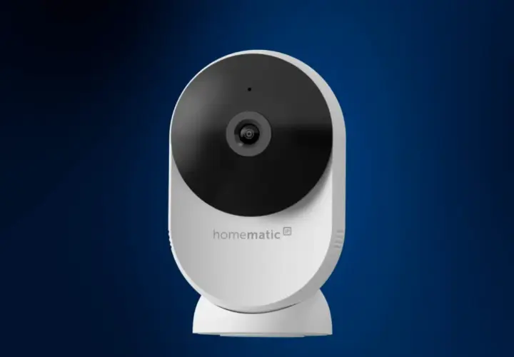 Weiße Homematic IP Überwachungskamera mit schwarzem Objektiv vor blauem Hintergrund.