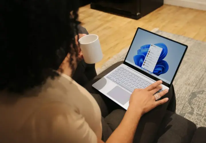 Person mit Tasse hält einen Laptop, auf dem Windows 11 installiert ist.