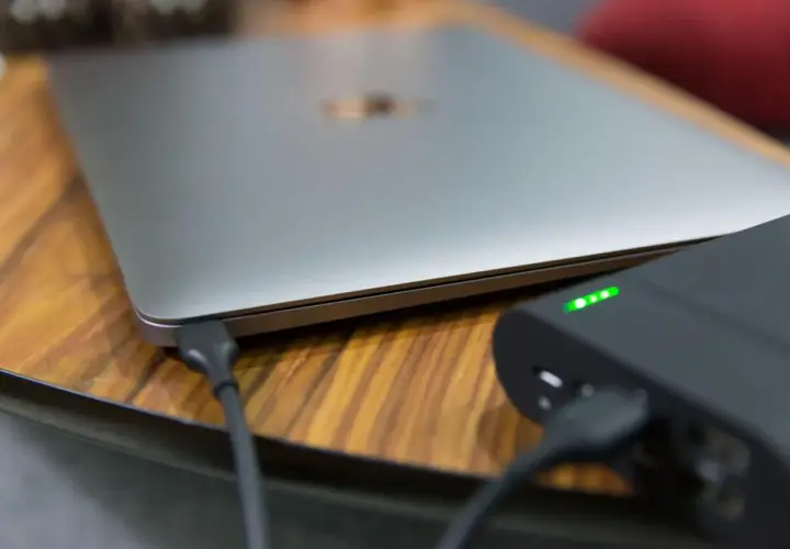 Ein Laptop wird mit einer Powerbank geladen. Die Ladeanzeige der Powerbank leuchtet grün.
