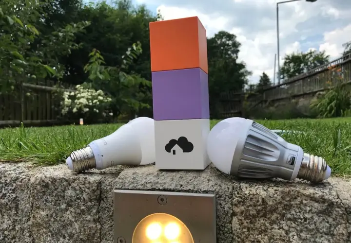 Zwei Glühbirnen liegen neben einem bunten Turm, der die Wahl zwischen Z-Wave vs. Zigbee symbolisiert.