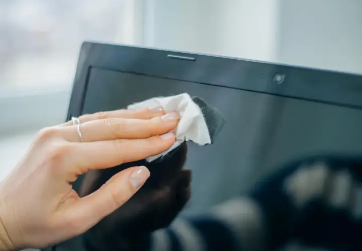 Eine Hand wischt mit einem Tuch den Laptop-Monitor reinigen.