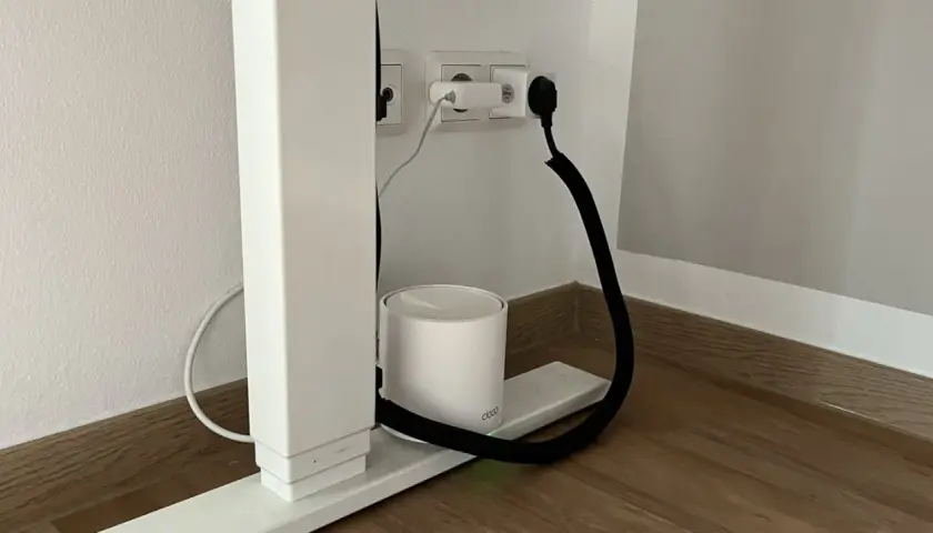 Ein weißer Router steht auf einem Sockel, während ein schwarzer Kabelkanal hilft, das Kabel unsichtbar zu verlegen.