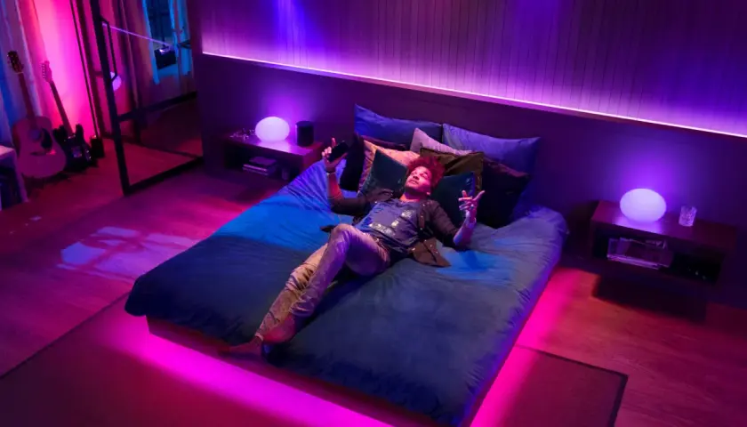 Mann liegt im Bett, umgeben von Philips Hue Lichtern, die sich im Takt von Spotify-Musik synchronisieren.
