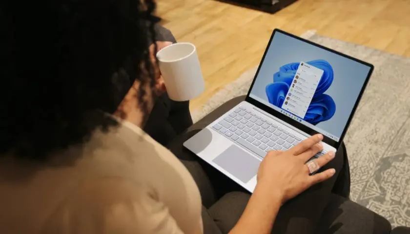 Person mit Tasse hält einen Laptop, auf dem Windows 11 installiert ist.