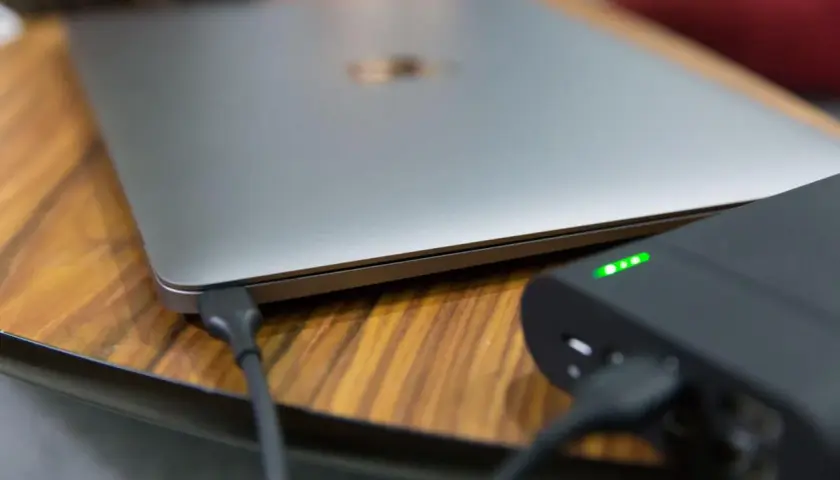 Ein Laptop wird mit einer Powerbank geladen. Die Ladeanzeige der Powerbank leuchtet grün.