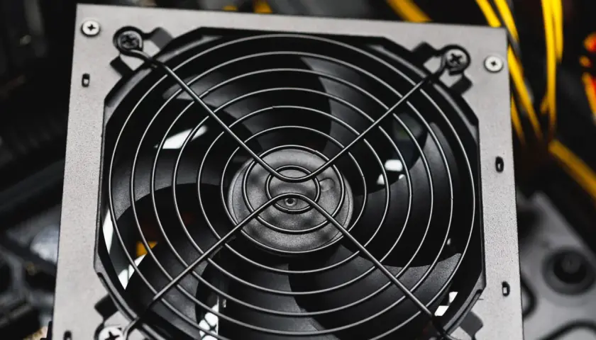 Nahaufnahme eines Lüfters eines PC-Netzteils, bereit für den psu test. Gelbe Kabel im Hintergrund.