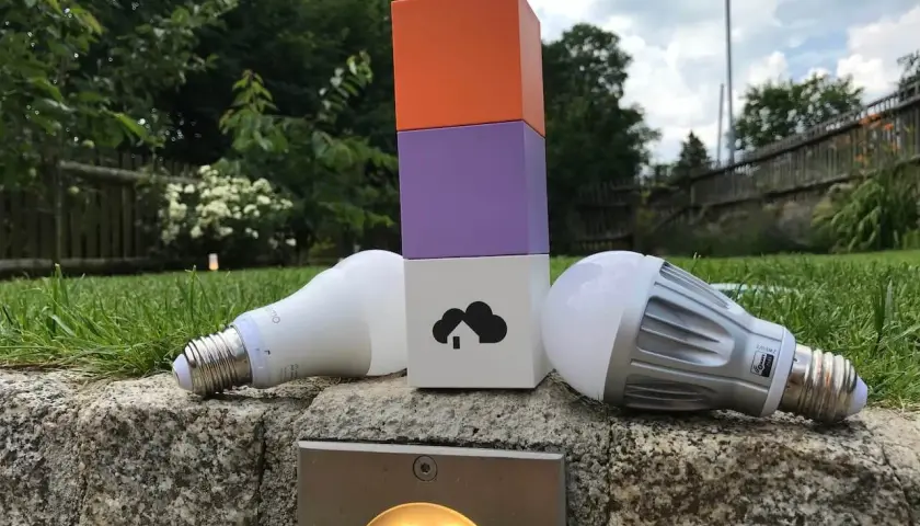 Zwei Glühbirnen liegen neben einem bunten Turm, der die Wahl zwischen Z-Wave vs. Zigbee symbolisiert.
