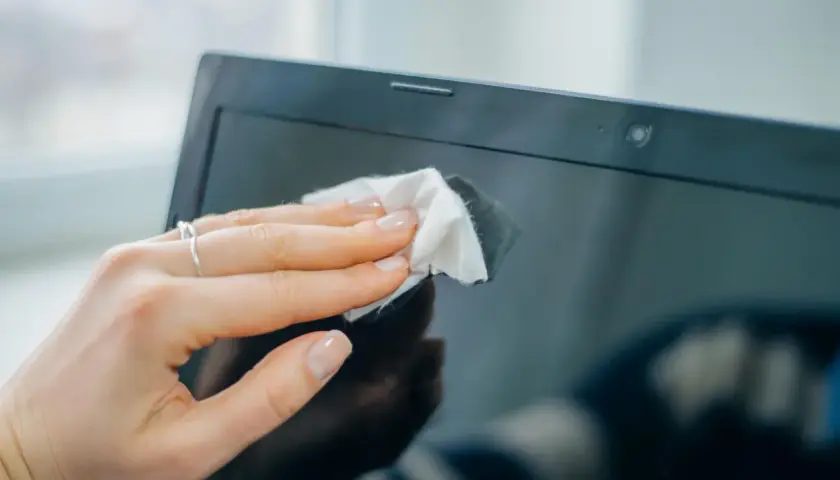 Eine Hand wischt mit einem Tuch den Laptop-Monitor reinigen.
