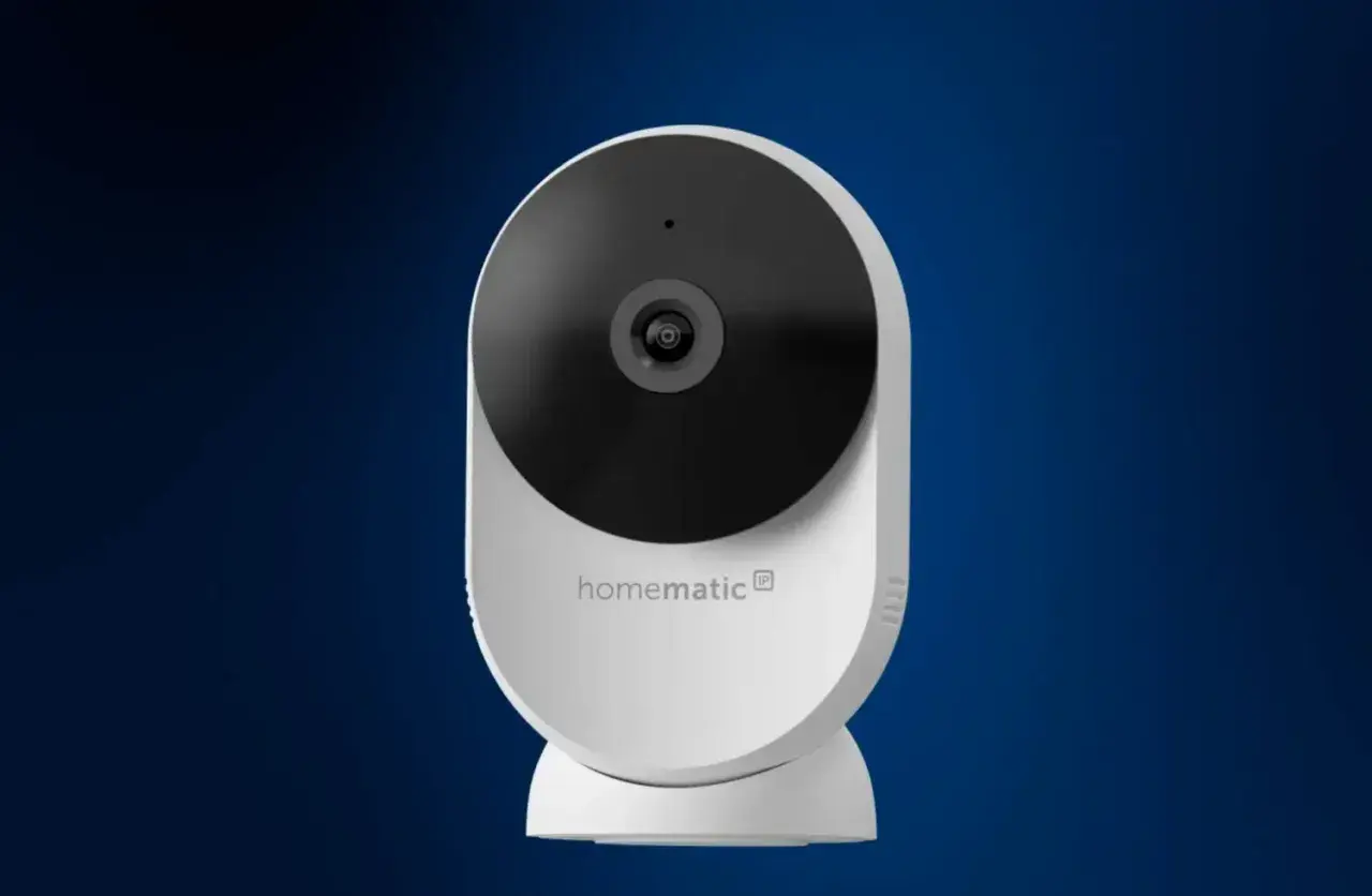 Weiße Homematic IP Überwachungskamera mit schwarzem Objektiv vor blauem Hintergrund.