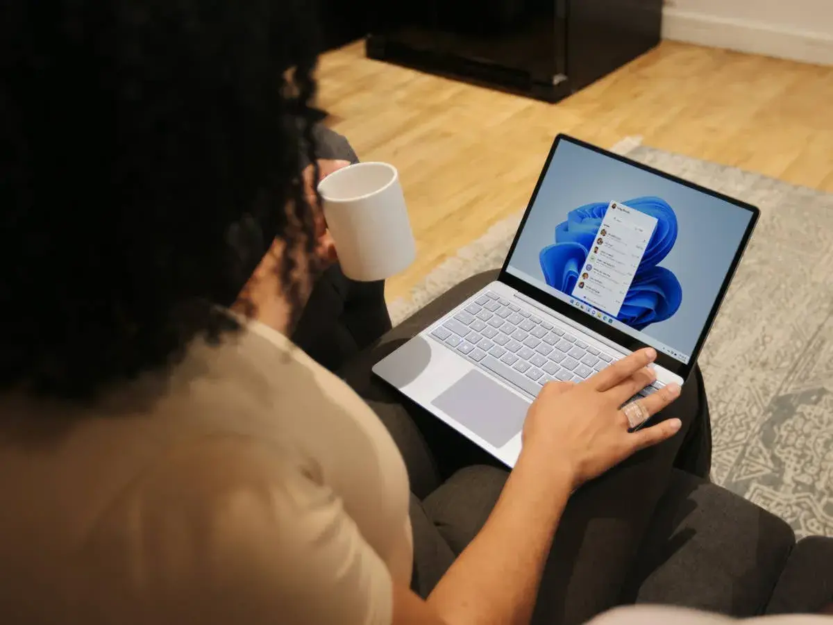 Person mit Tasse hält einen Laptop, auf dem Windows 11 installiert ist.