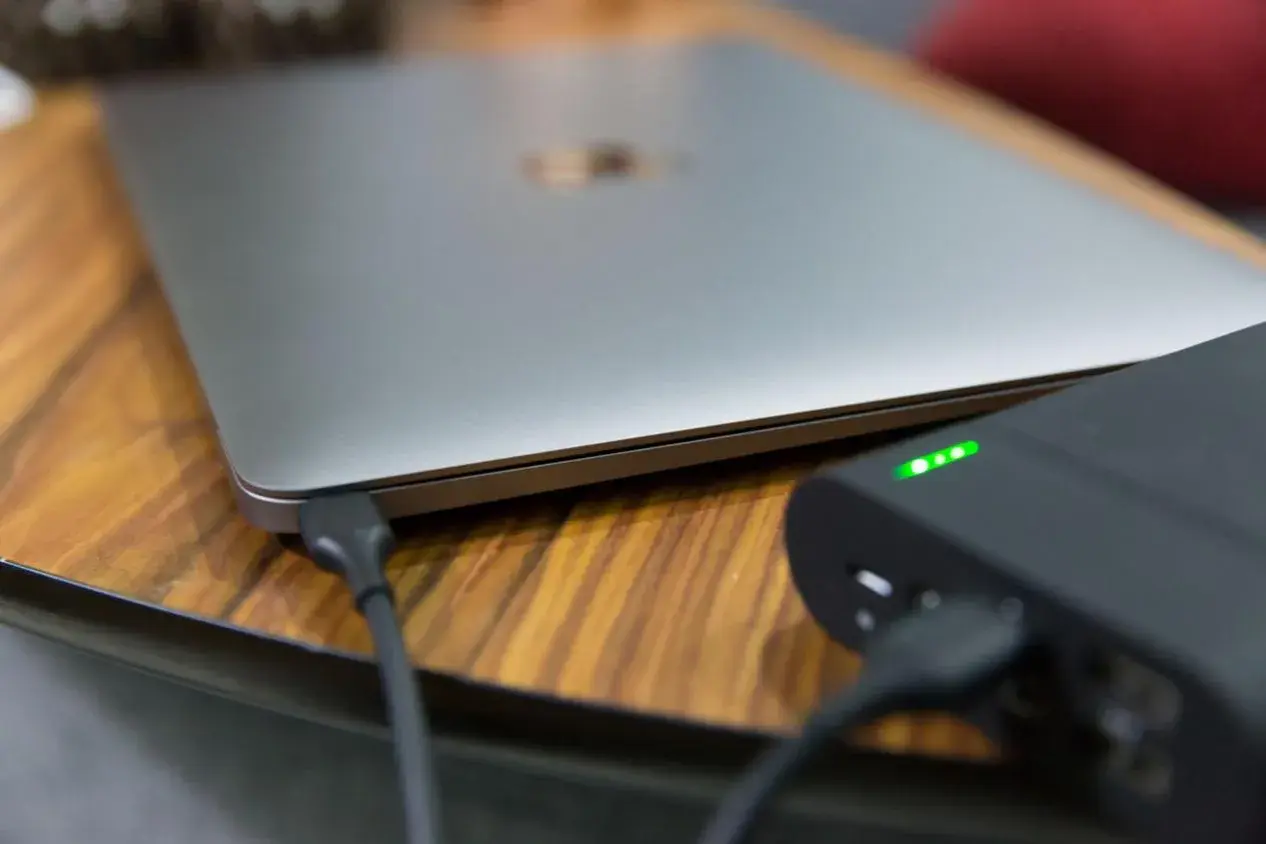 Ein Laptop wird mit einer Powerbank geladen. Die Ladeanzeige der Powerbank leuchtet grün.