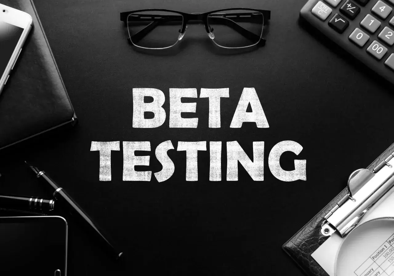 BETA TESTING: Ein Smartphone, Brille und ein Taschenrechner liegen neben der Aufschrift. Die offene Beta-Phase beginnt.
