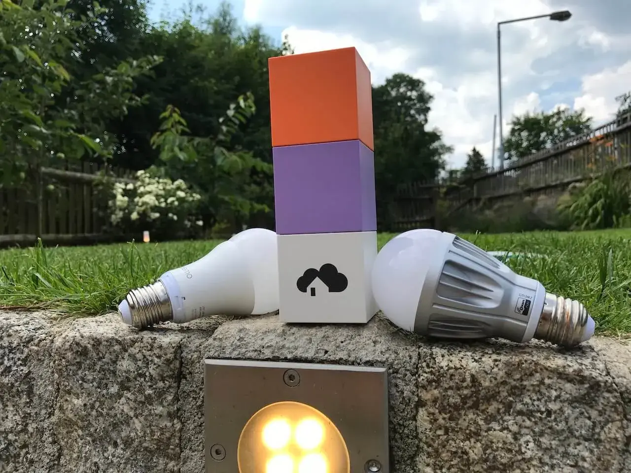 Zwei Glühbirnen liegen neben einem bunten Turm, der die Wahl zwischen Z-Wave vs. Zigbee symbolisiert.