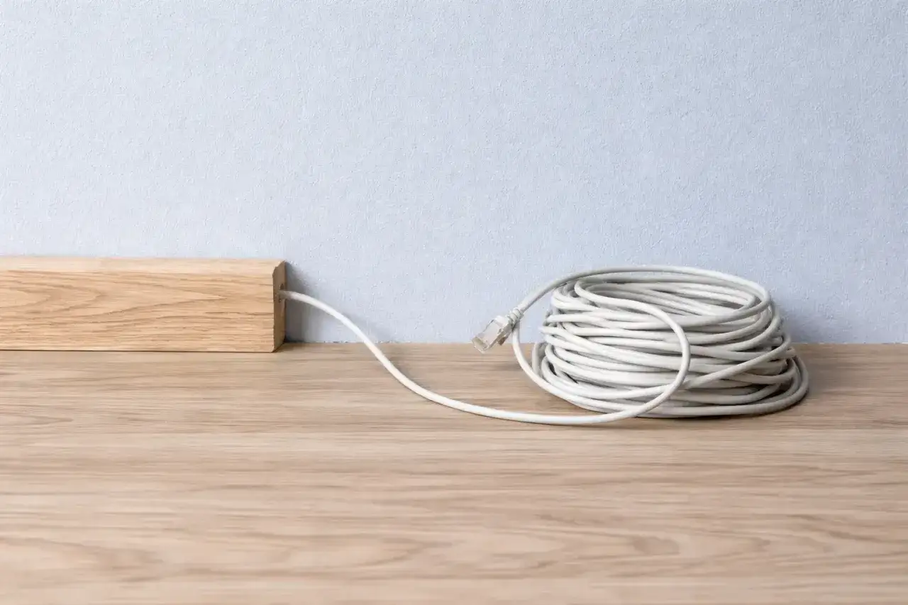 Ein Holzelement verdeckt ein Kabel, um es unsichtbar zu verlegen. Daneben liegt eine aufgerollte wei&szlig;e Kabeltrommel.