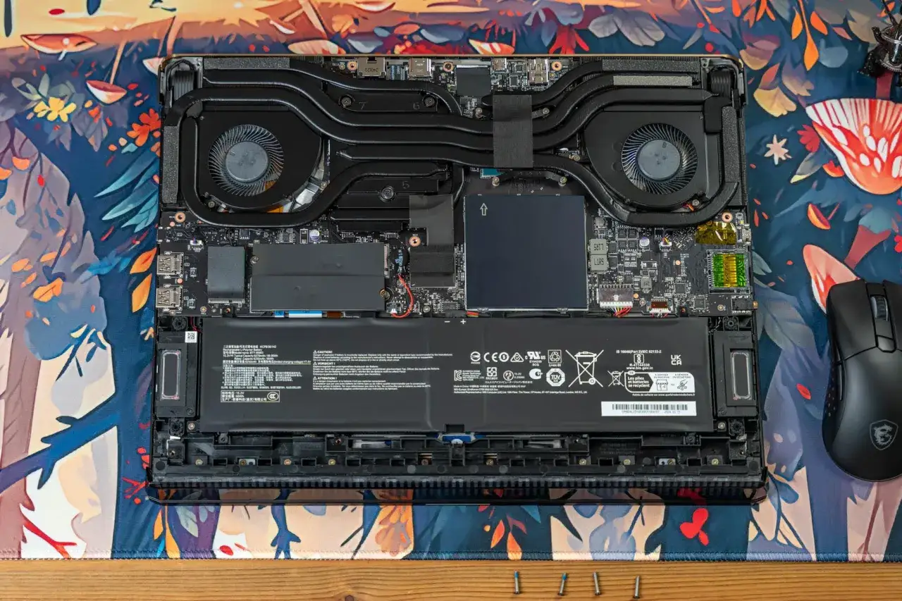 Laptop-Innenleben für ein Upgrade: Akku, Lüfter und Hauptplatine sind sichtbar. Ein Gaming-Maus liegt daneben.