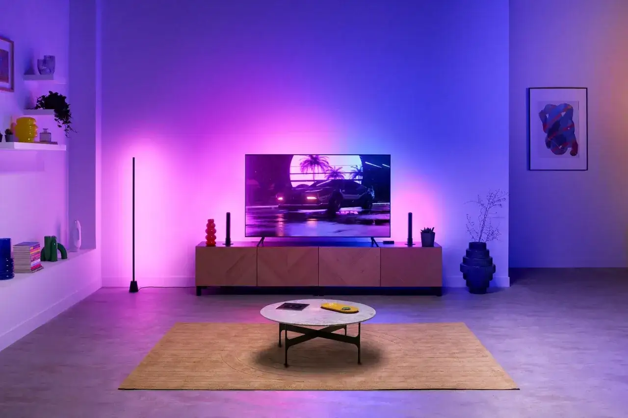 Modernes Wohnzimmer mit einem Fernseher, der ein Auto-Motiv zeigt, umgeben von stimmungsvollem lg ambilight in Lila- und Blaut&ouml;nen.